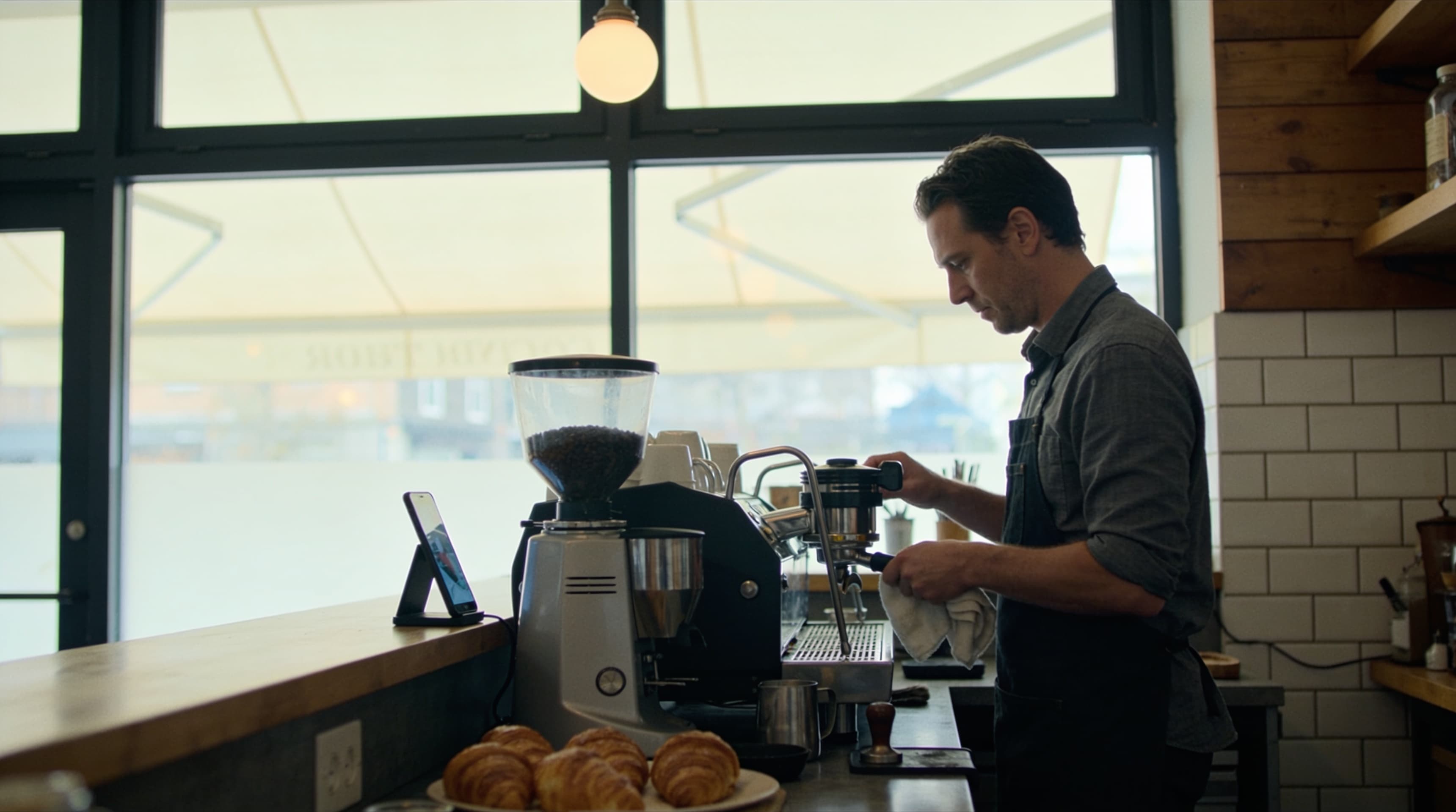 A cafe owner checking their phone beside the espresso machine in the morning